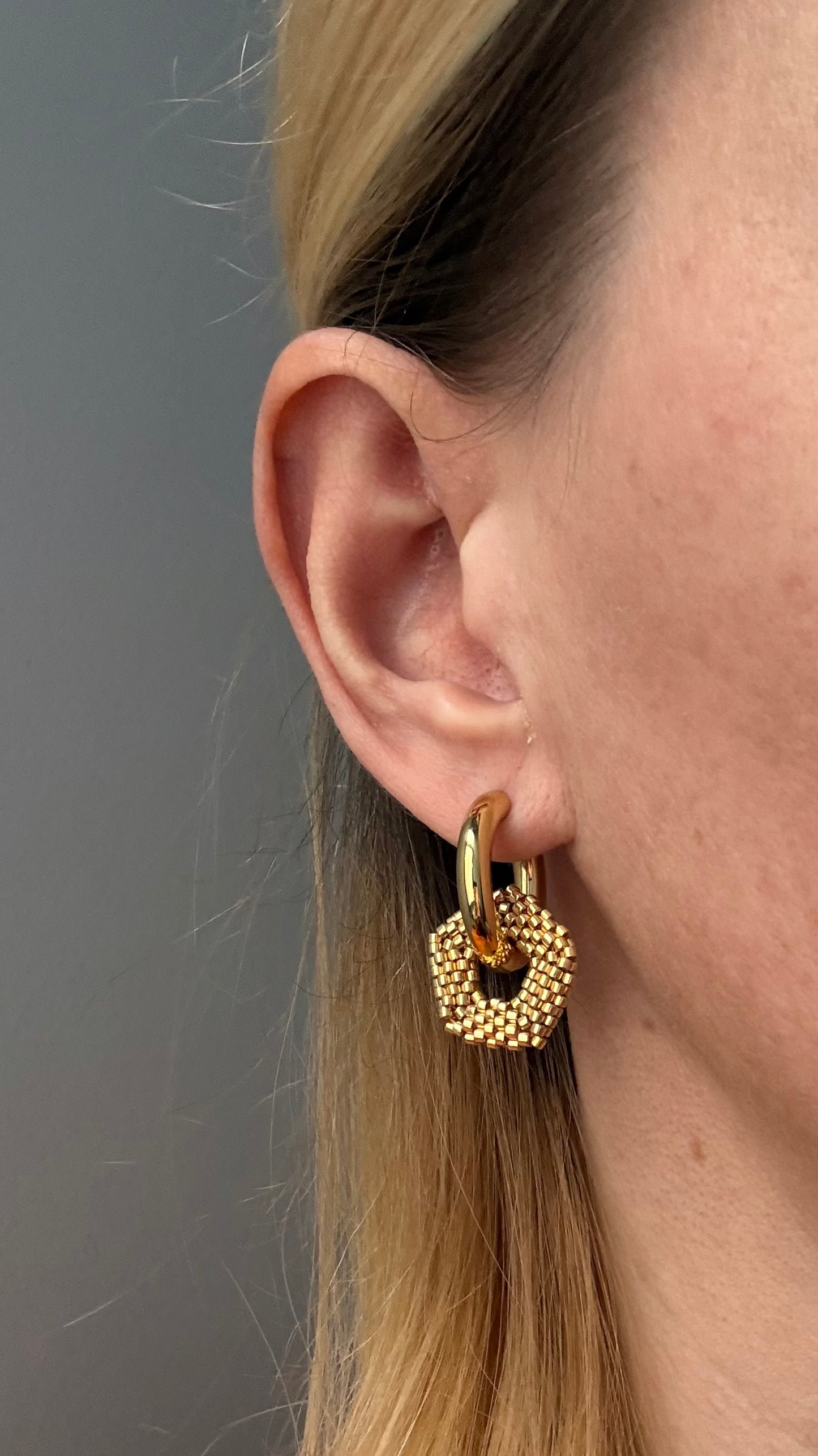 Gold hoop earrings with a textured charm worn by a person against a neutral background