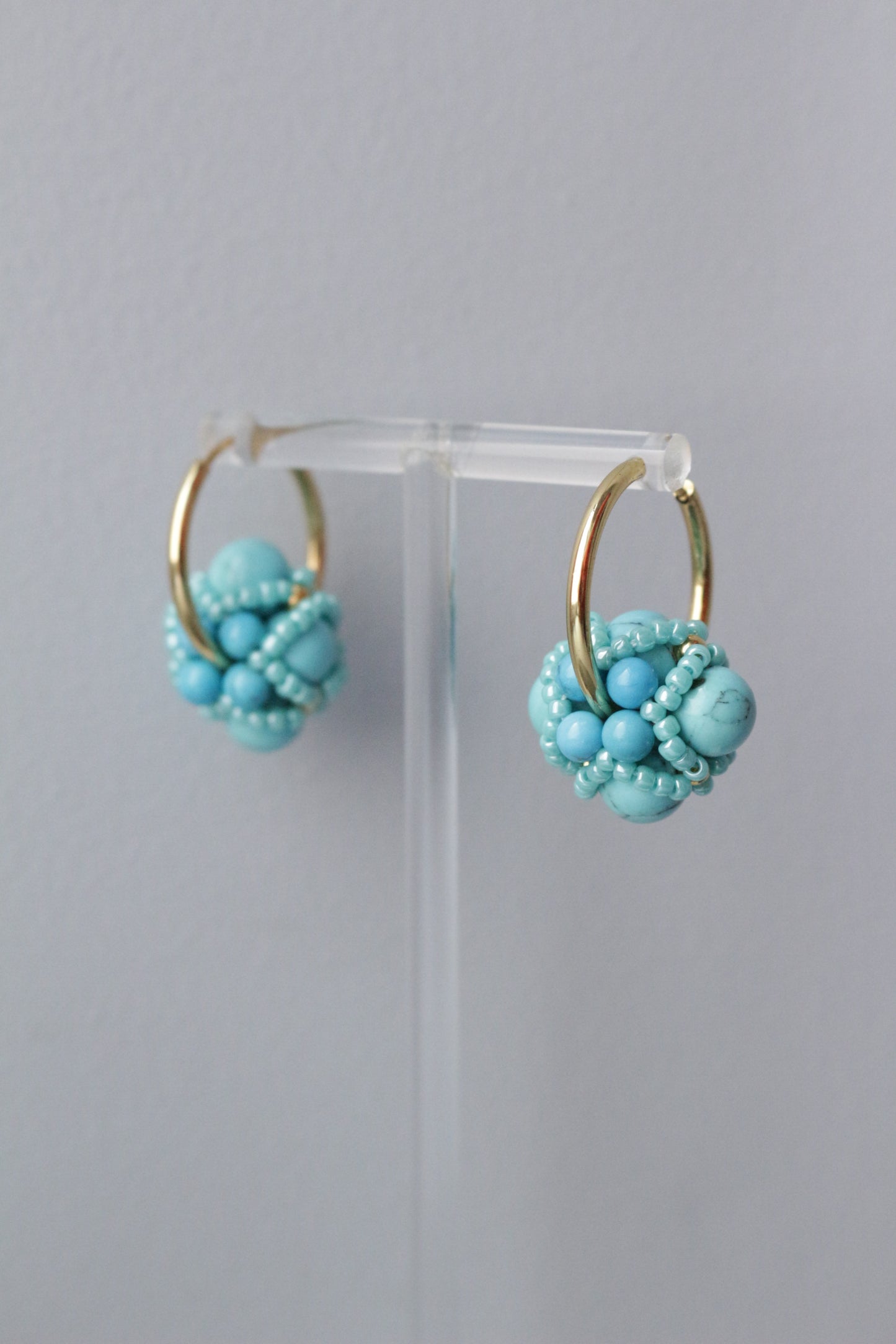 Turquoise beaded pendants on a clear stand against a grey background