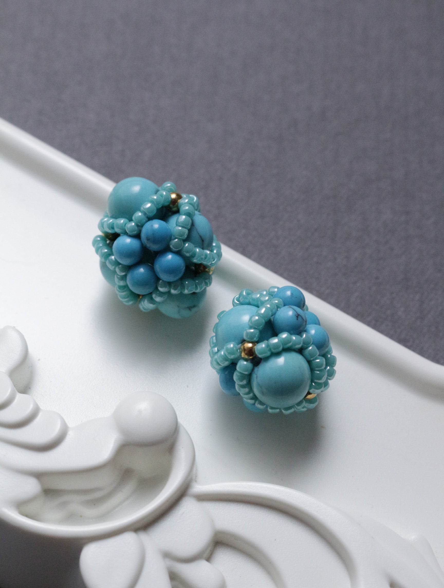 Pair of turquoise beaded element on a decorative white surface.