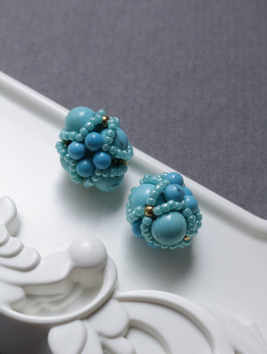 Pair of turquoise beaded element on a decorative white surface.