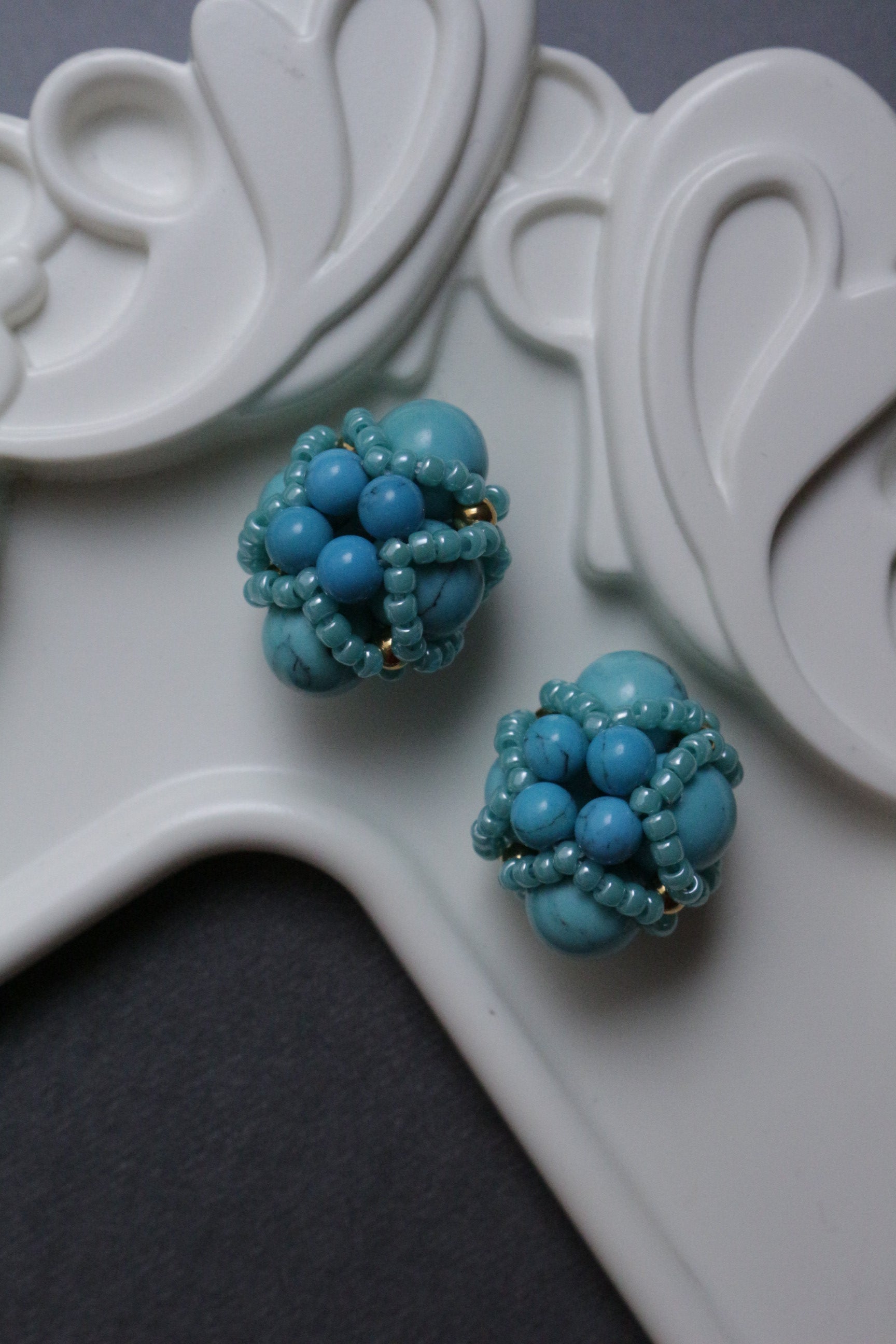 Turquoise beaded element on a white decorative stand.
