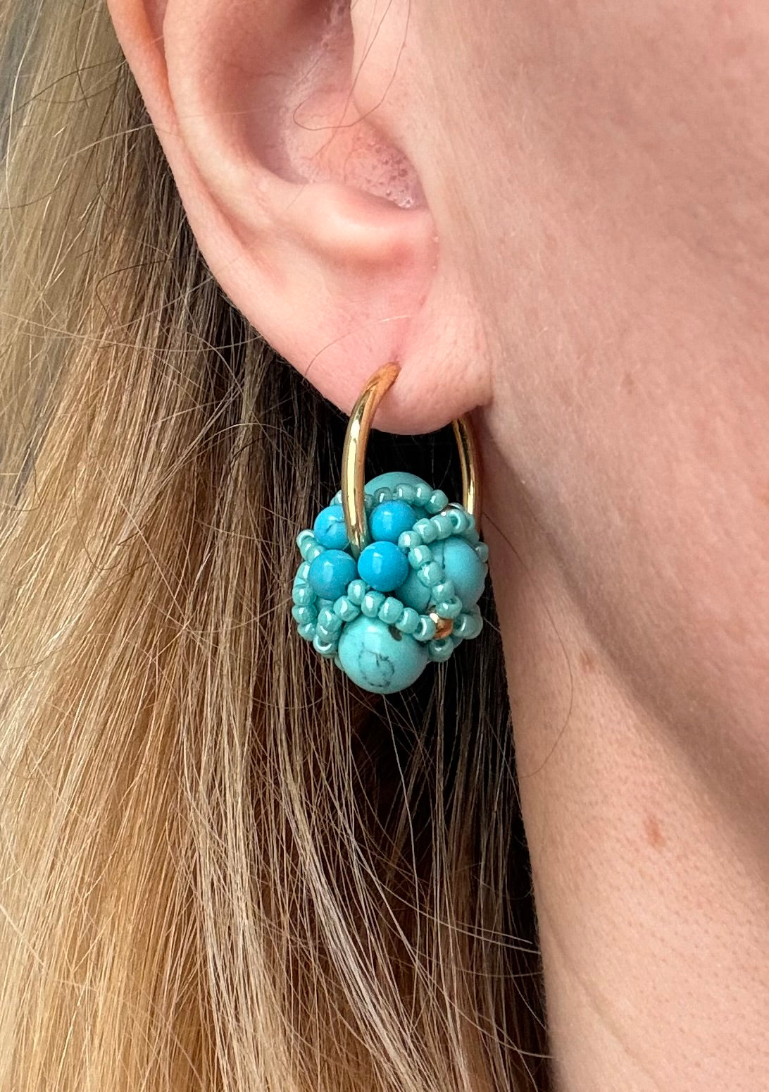 Close-up of an ear wearing a turquoise beaded earring with gold accents.