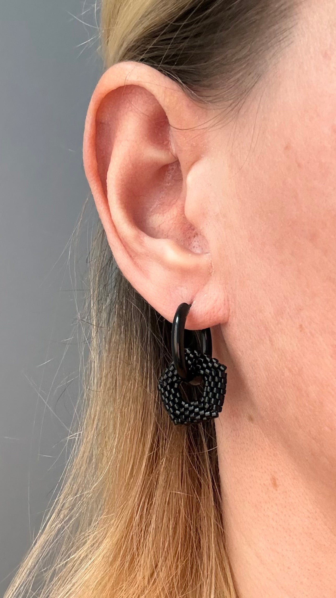Close-up of an ear wearing a black hoop earring with a textured design against a neutral background.