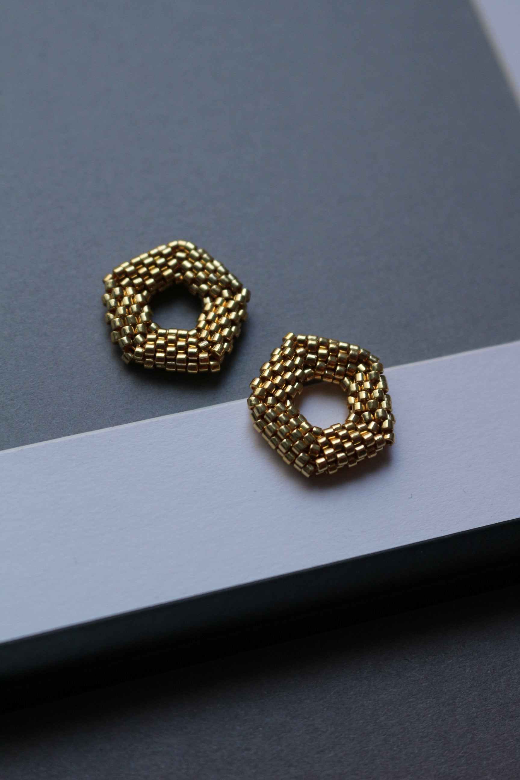 Gold pendant earrings on a gray and black background