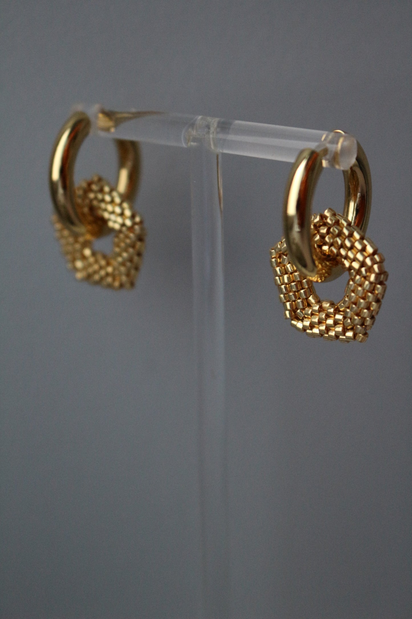 Gold earrings on a clear stand against a gray background